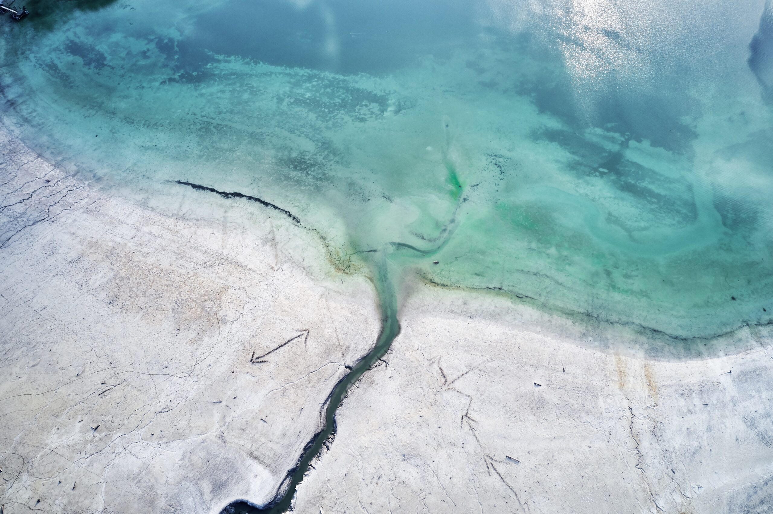 A high angle shot of the turquoise water of the sea next to the shore with engravings of arrows